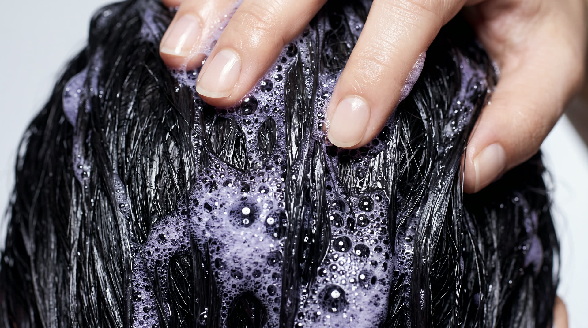Fingertips massaging violet lather into wet hair